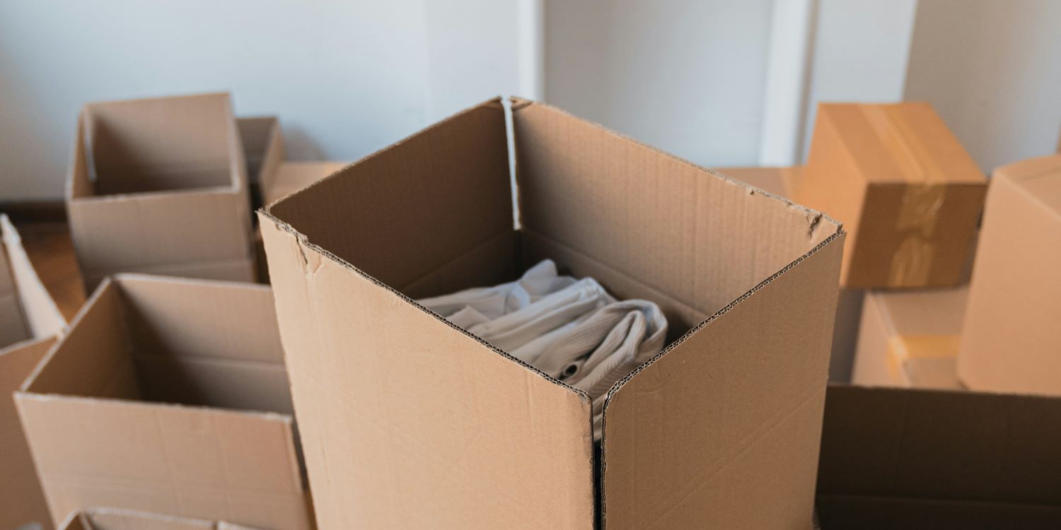 Carton ouvert rempli de vêtements pliés, entouré de cartons en attente, prêt pour l’emballage lors d’un déménagement. Comment préparer son déménagement etape par étape.