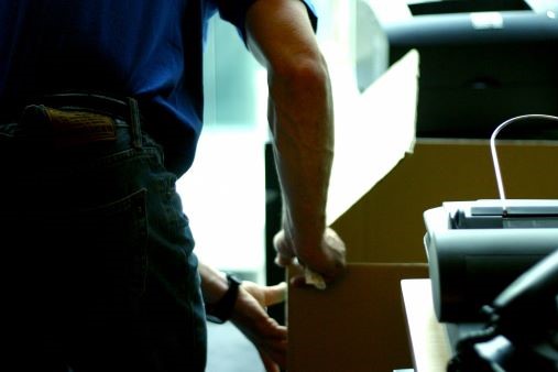 Deux personnes manipulant des cartons et déménageant des objets lourds près d'une imprimante; ambiance travail et organisation du déménagement. Comment bien organiser son déménagement est évoqué par le contexte.